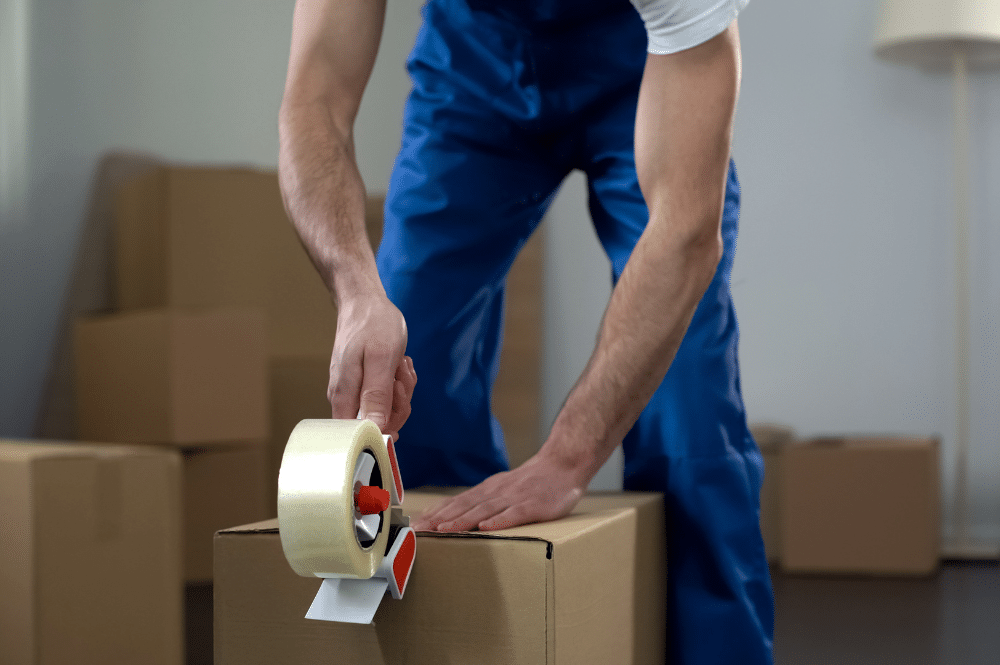 A man in overalls holds a roll of tape, ready for packing services related to moving.